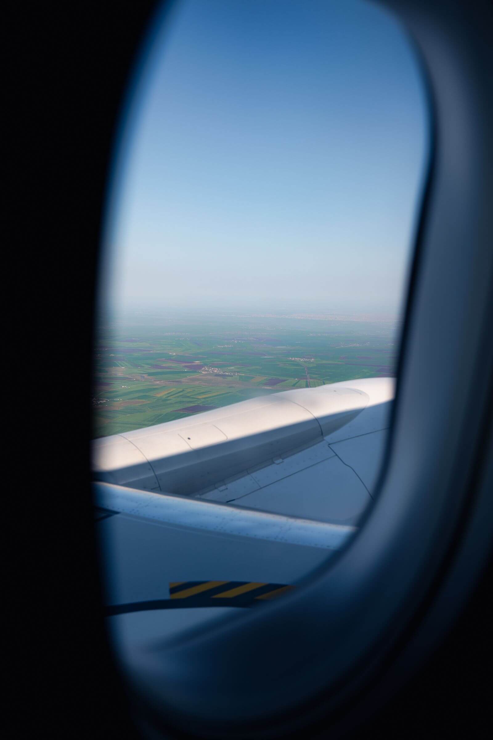 View of airplane engine and wing above green farmland